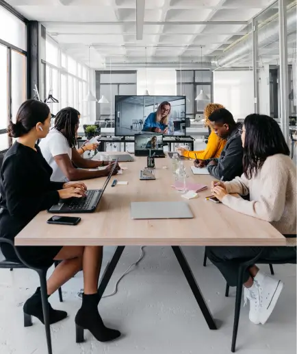 People are sitting around a conference room table with their heads turned towards a large TV screen.